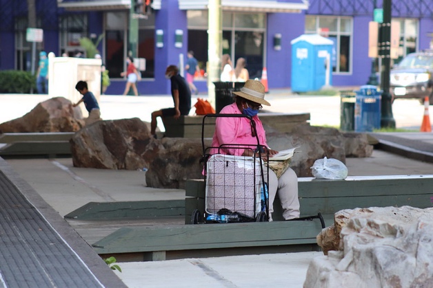 A person experiencing homelessness sitting on a bench in a city